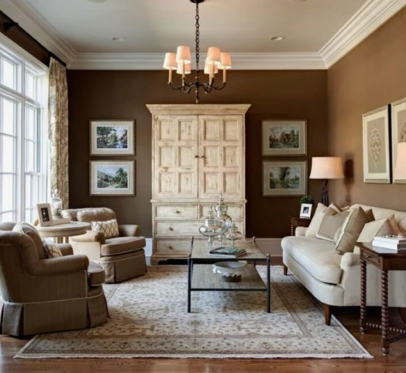 A cozy living room with brown walls, a cream armoire, a patterned rug, and a small chandelier.