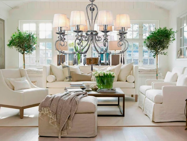 A bright, cream-colored living room featuring a large chrome chandelier with white lampshades.