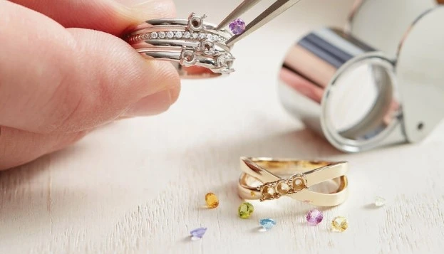 Close-up of a jeweler using tweezers to set a small purple stone into a silver ring setting.