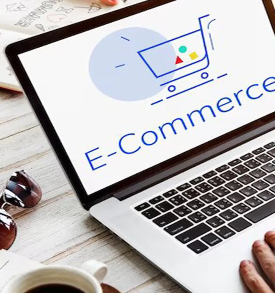 A close-up, angled shot of a person's hand on a laptop keyboard; the screen displays a minimalist shopping cart illustration and the word "E-Commerce."